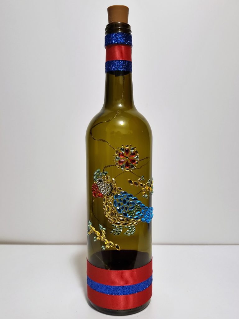 Bottle light featuring a jewelled parrot and red and blue ribbons.