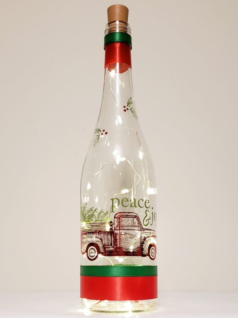 Bottle light featuring a metallic red truck carrying a Christmas tree, and the words, "Peace and Joy".