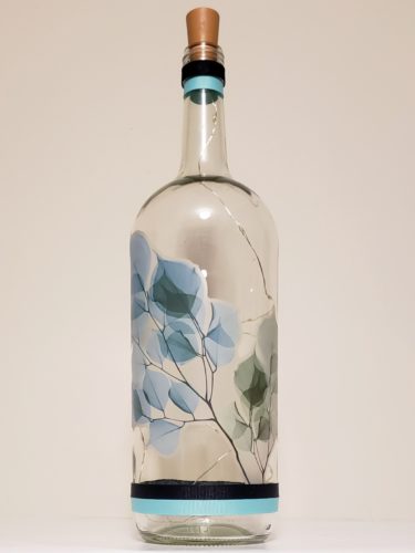 Bottle light with a large branch with green-blueish leaves wrapping around it.